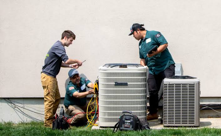 Three technicians working with residential outdoor air conditioning equipment