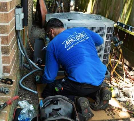 Technician troubleshooting an outdoor air conditioning unit beside a brick home